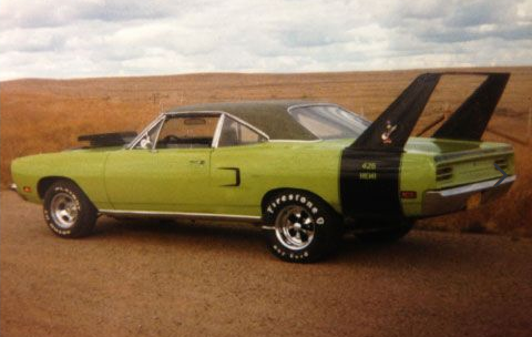 A green car with a black wing is parked on a dirt road