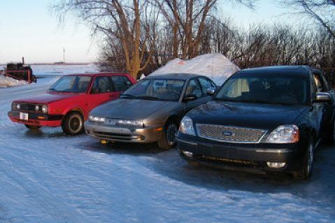 Three cars are parked in the snow on a snowy road.
