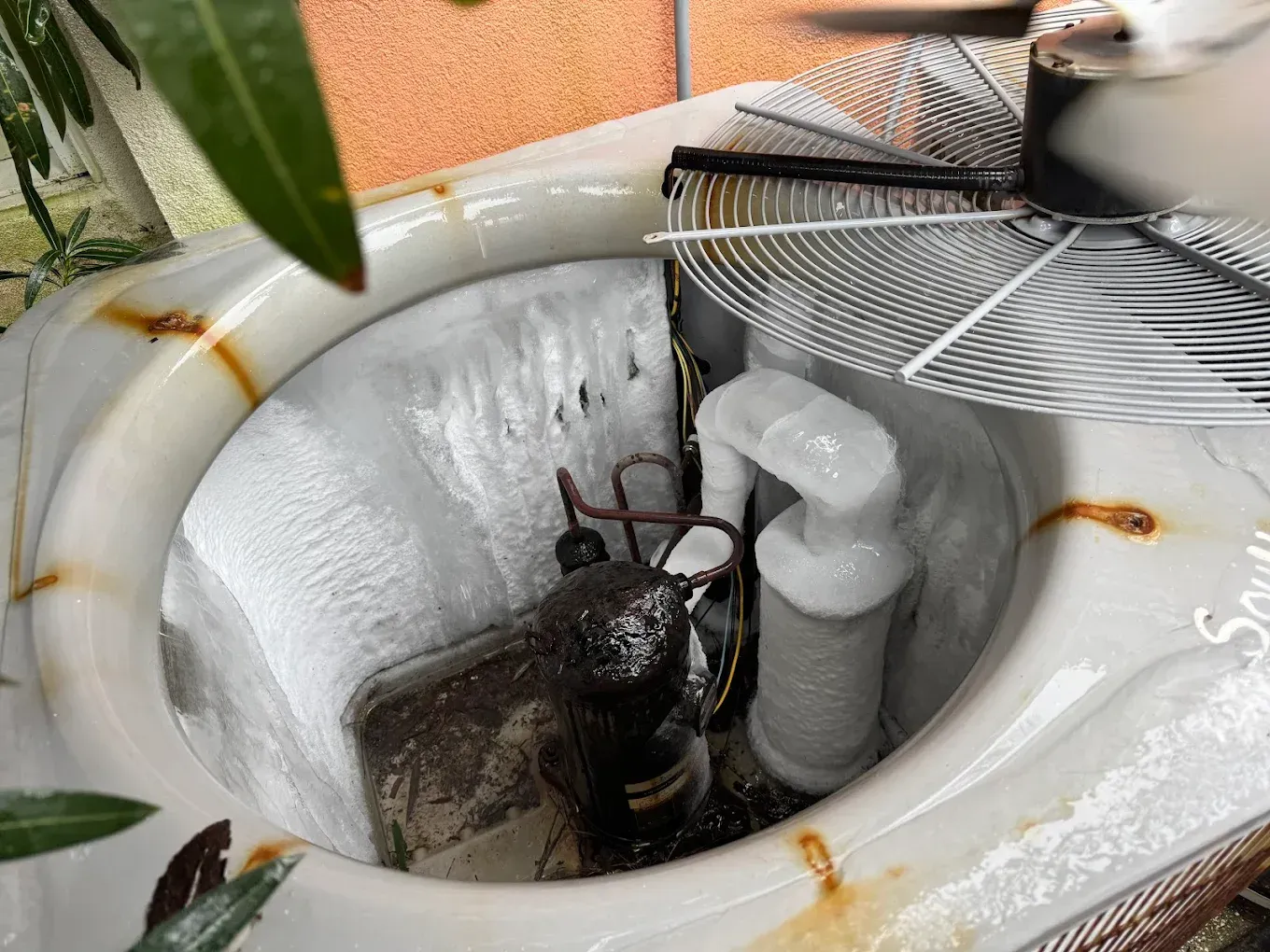 Frozen toilet tank with visible components, rust stains, and fan partially visible.