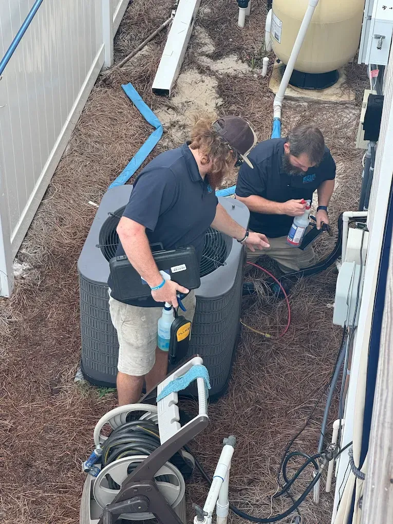 Two people in blue shirts examine a hot tub outside near a white fence.