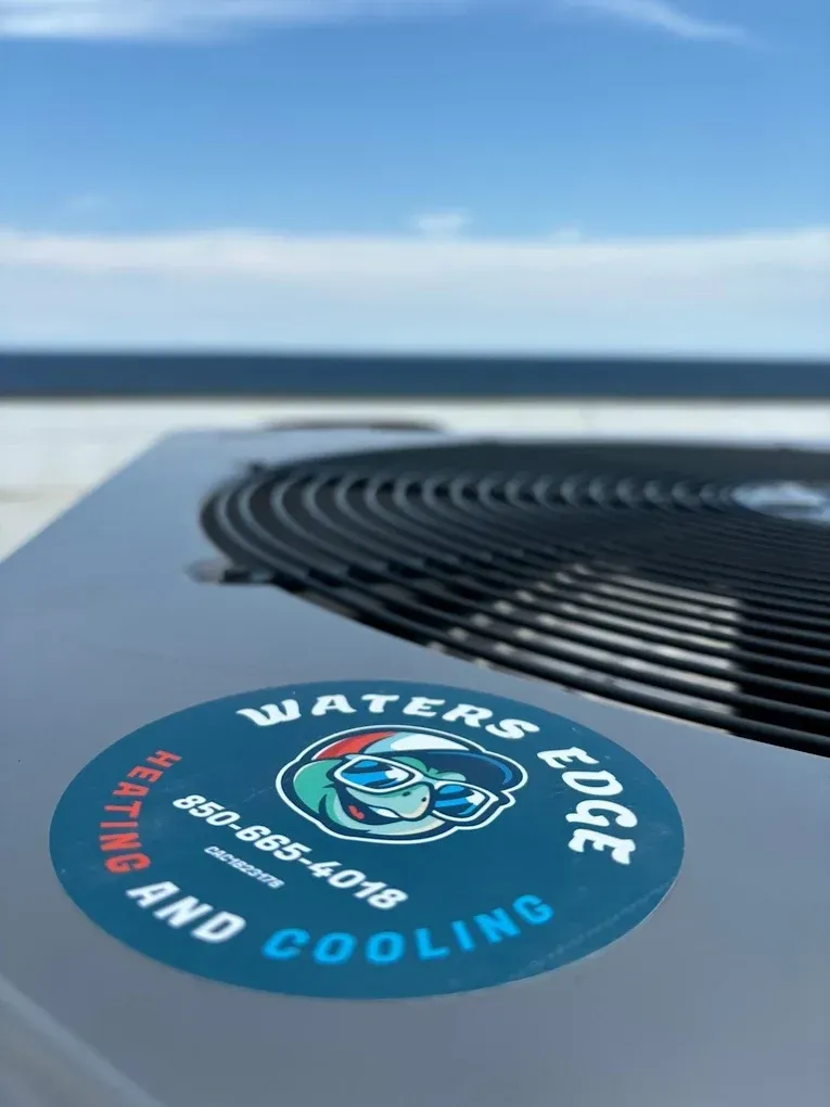Air conditioning unit with Waters Edge Heating and Cooling logo, ocean background, sunny sky.