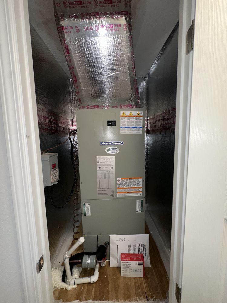 HVAC unit installed in a closet, with ductwork, water pipes, and electrical components. Silver and white tones dominate.