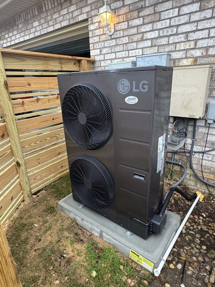 LG heat pump unit on a concrete pad next to a brick wall and wooden fence.