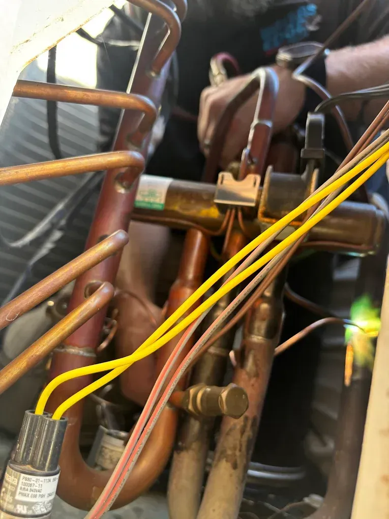 HVAC technician working on copper pipes and valve with electrical wires.