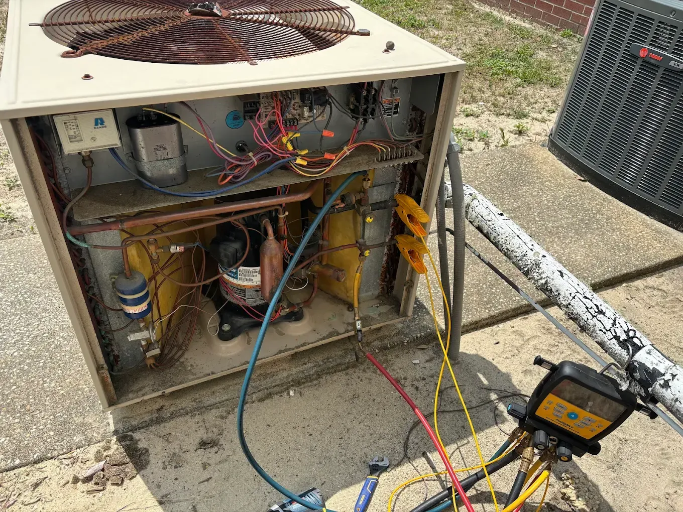 Open air conditioning unit with exposed wiring, copper tubing, and gauges.