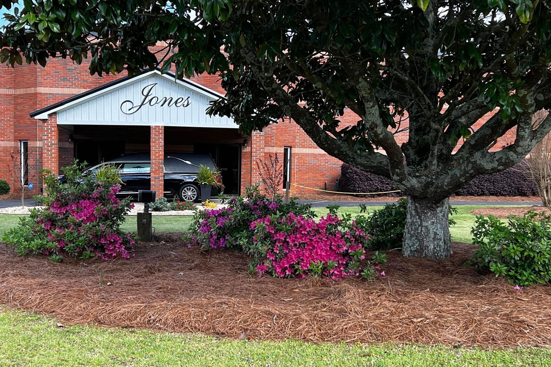 A brick building with a car parked in front of it and a tree in front of it.