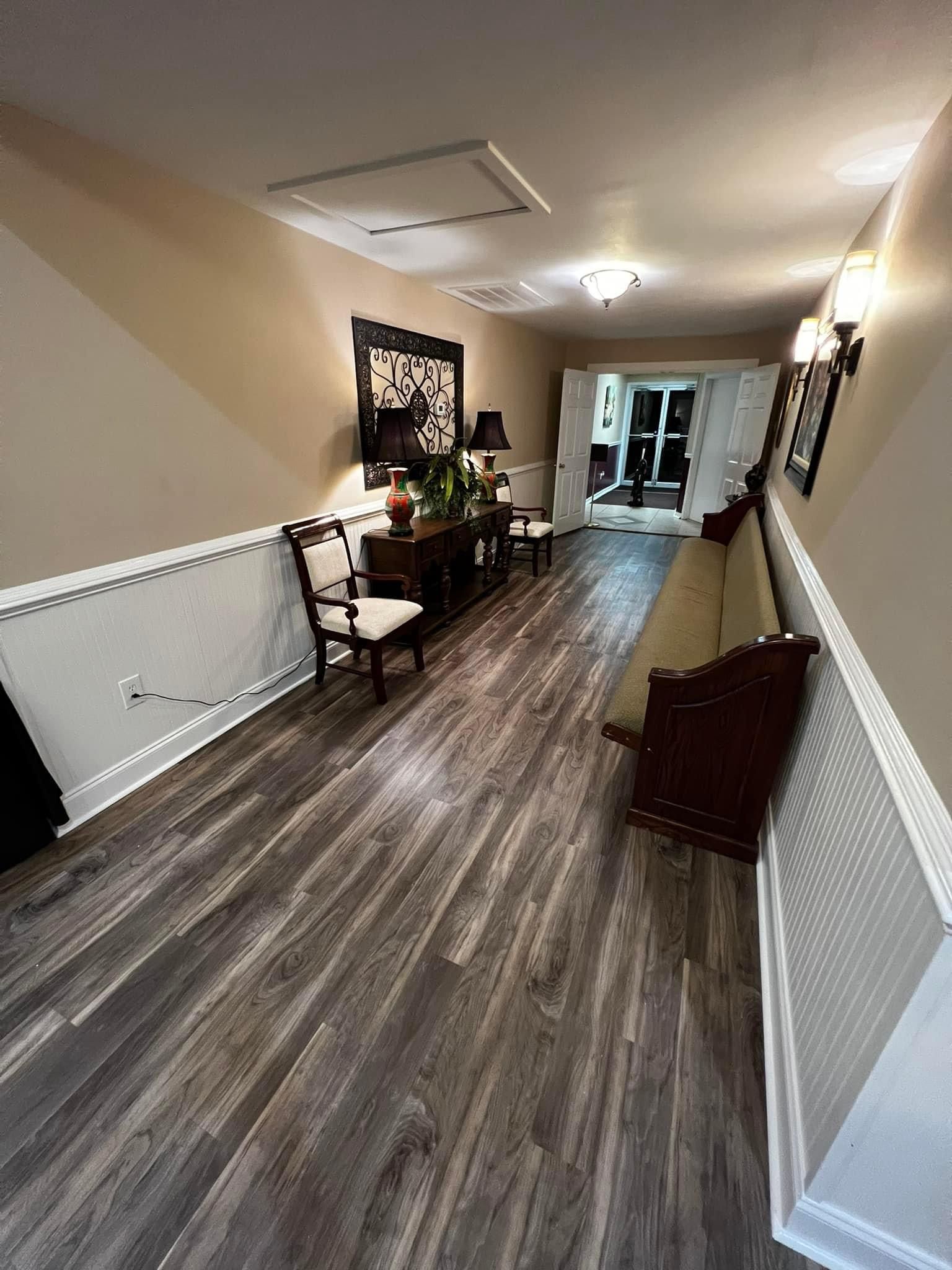 A long hallway with wooden floors and chairs in a house.