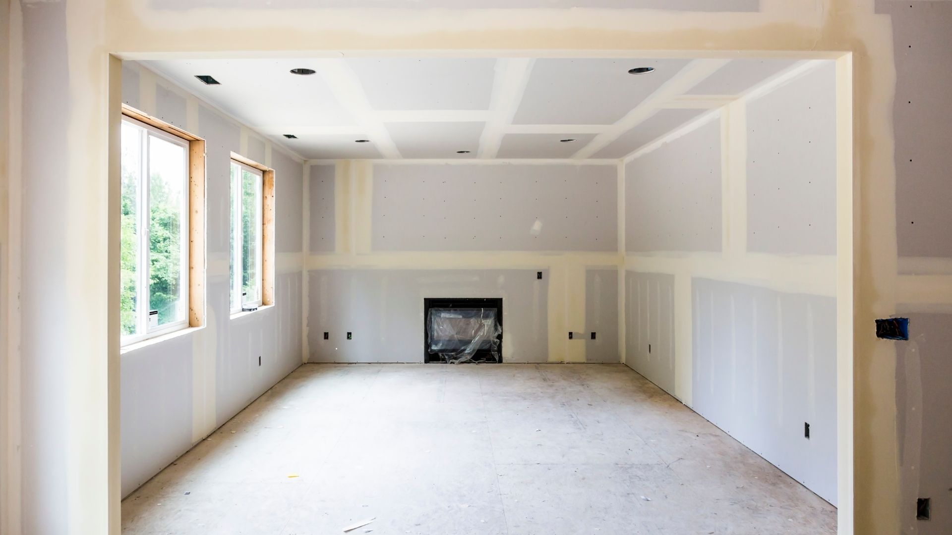 Interior room under construction with drywall, windows, and a fireplace.