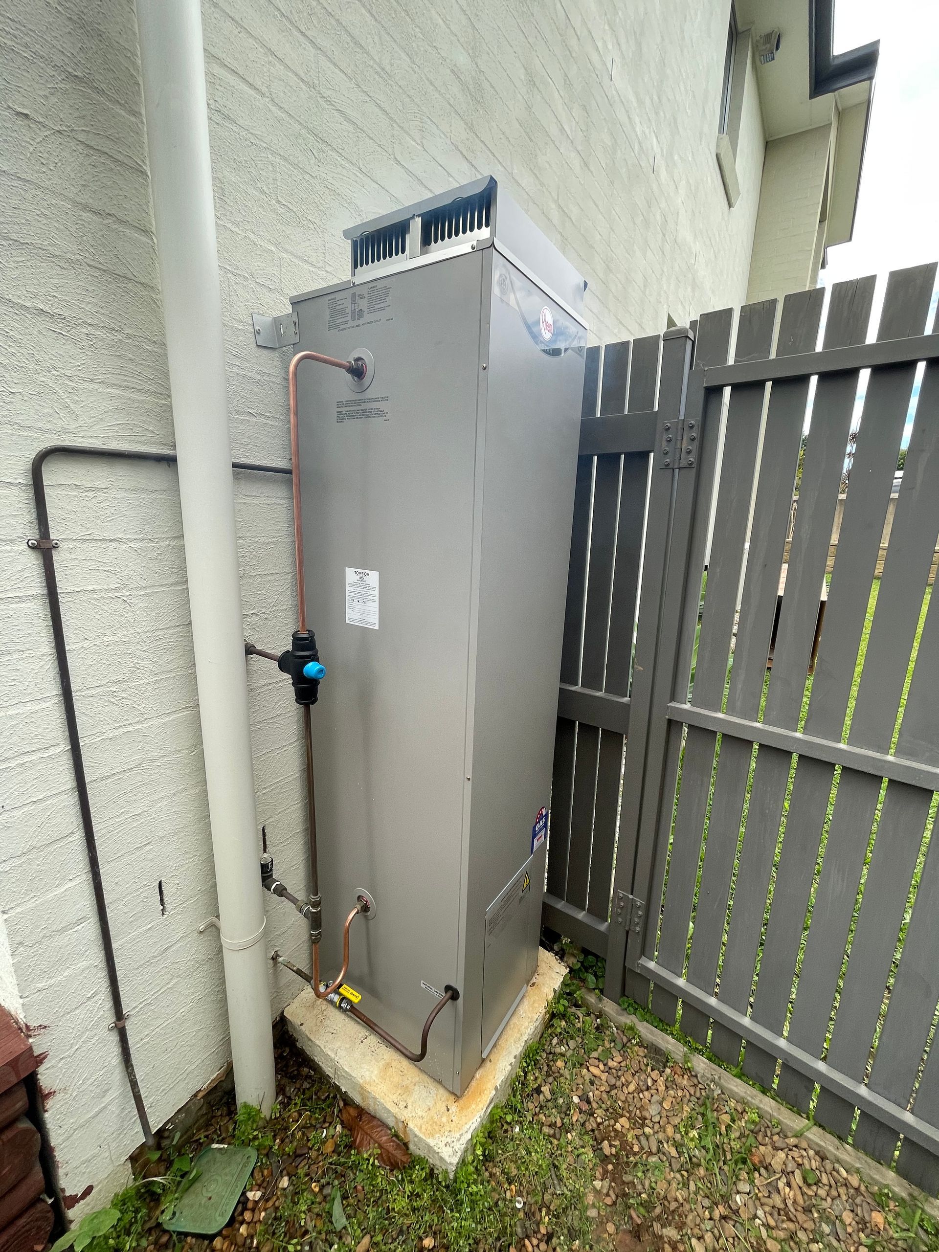 Gray Air Conditioning Unit Next to a Fence and House Wall — Start 2 Finish Plumbing in Cronulla, NSW