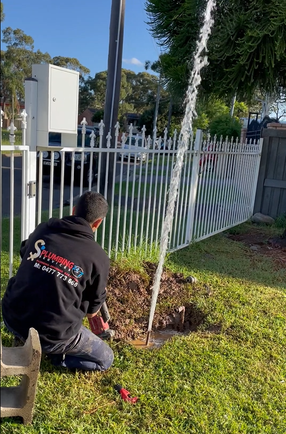 Man Repairing a Water Pipe Gushing Water, Near a Fence and Utility Pole — Start 2 Finish Plumbing in Greenacre, NSW