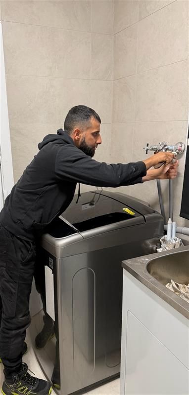 Man washing hands at a utility sink beside a stainless steel laundry machine. — Start 2 Finish Plumbing in Yagoona, NSW