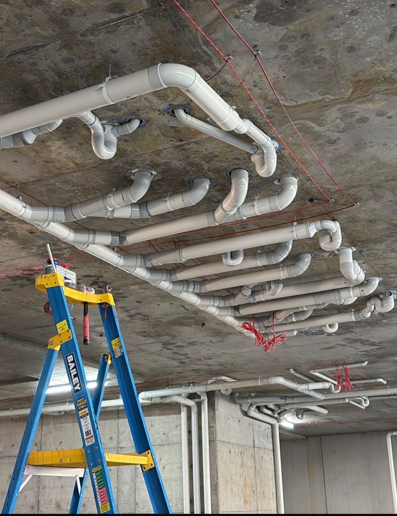 Blue and yellow ladder beneath white ceiling pipes in an unfinished room — Start 2 Finish Plumbing in Yagoona, NSW