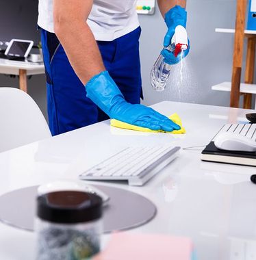 A man in blue gloves is cleaning a desk with a spray bottle