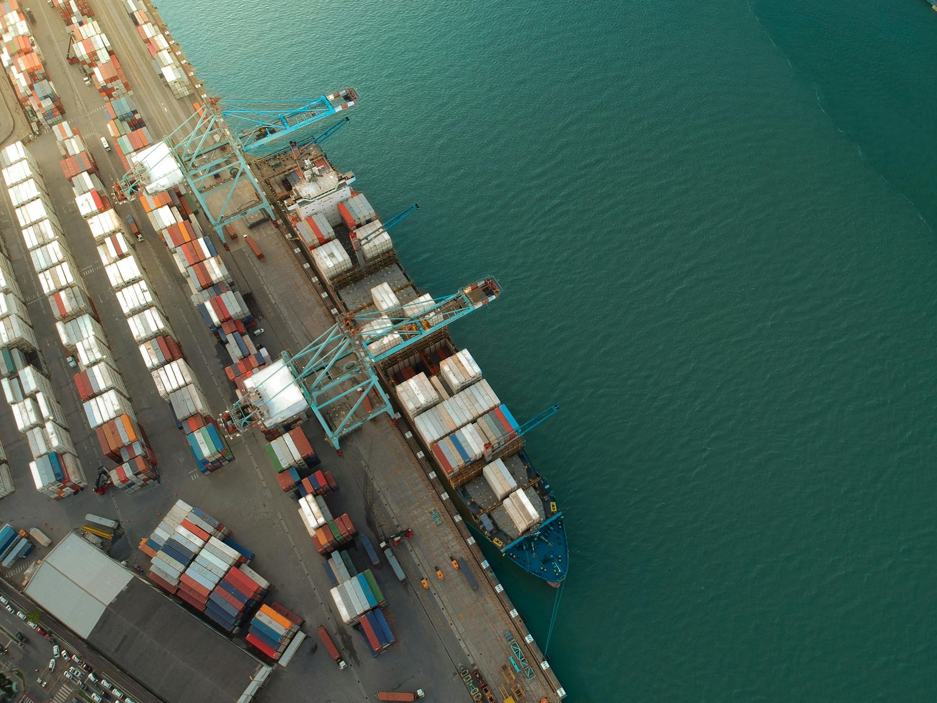 A cargo shipped docked at a port with cargo containers on the port and ship