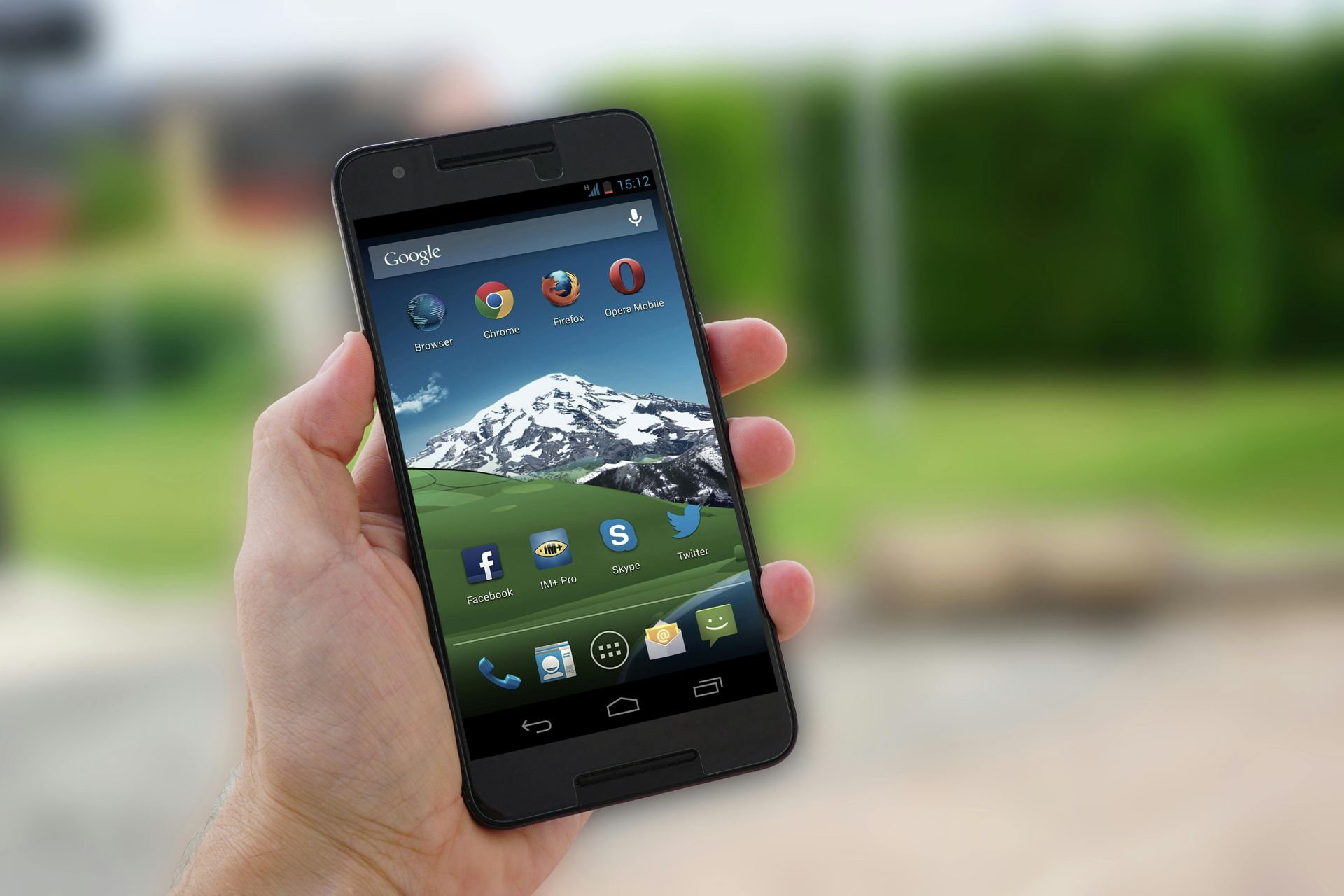Hand holding a black smartphone with mountain wallpaper, outdoors.