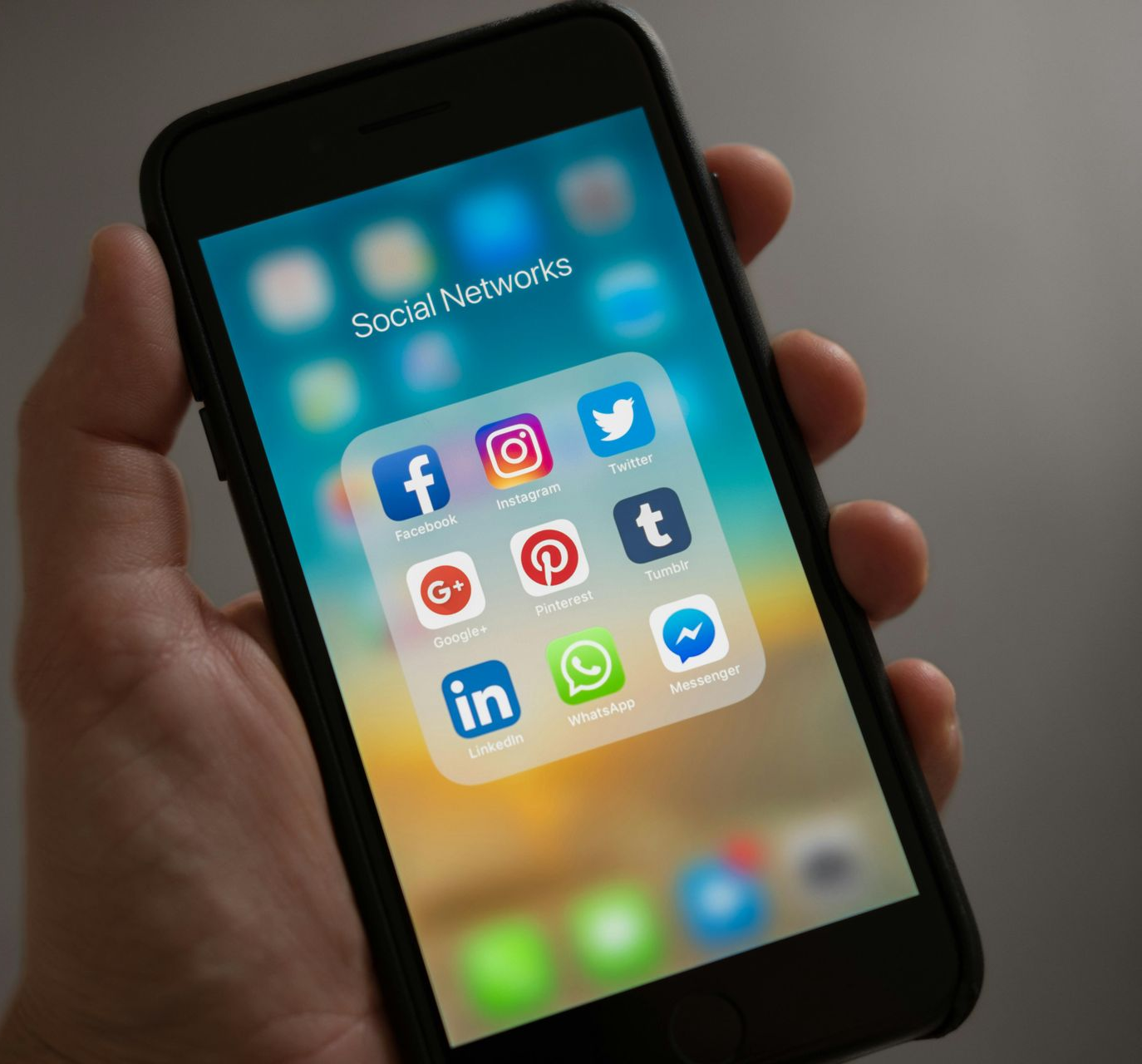 Hand holding a smartphone displaying social media app icons, including Facebook, Instagram, Twitter, and Pinterest.