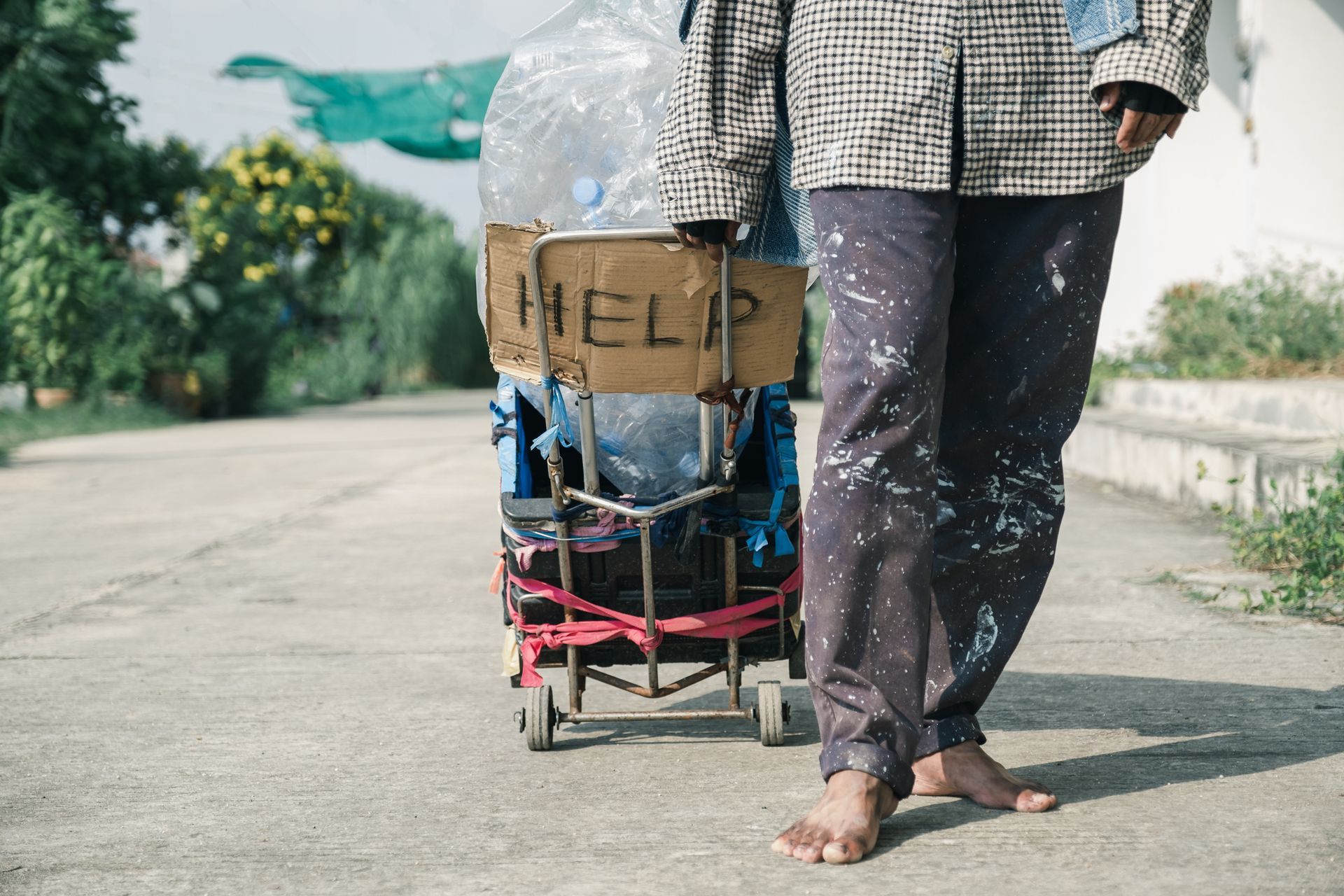 Homeless person with bare feet stands next to a cart with a 