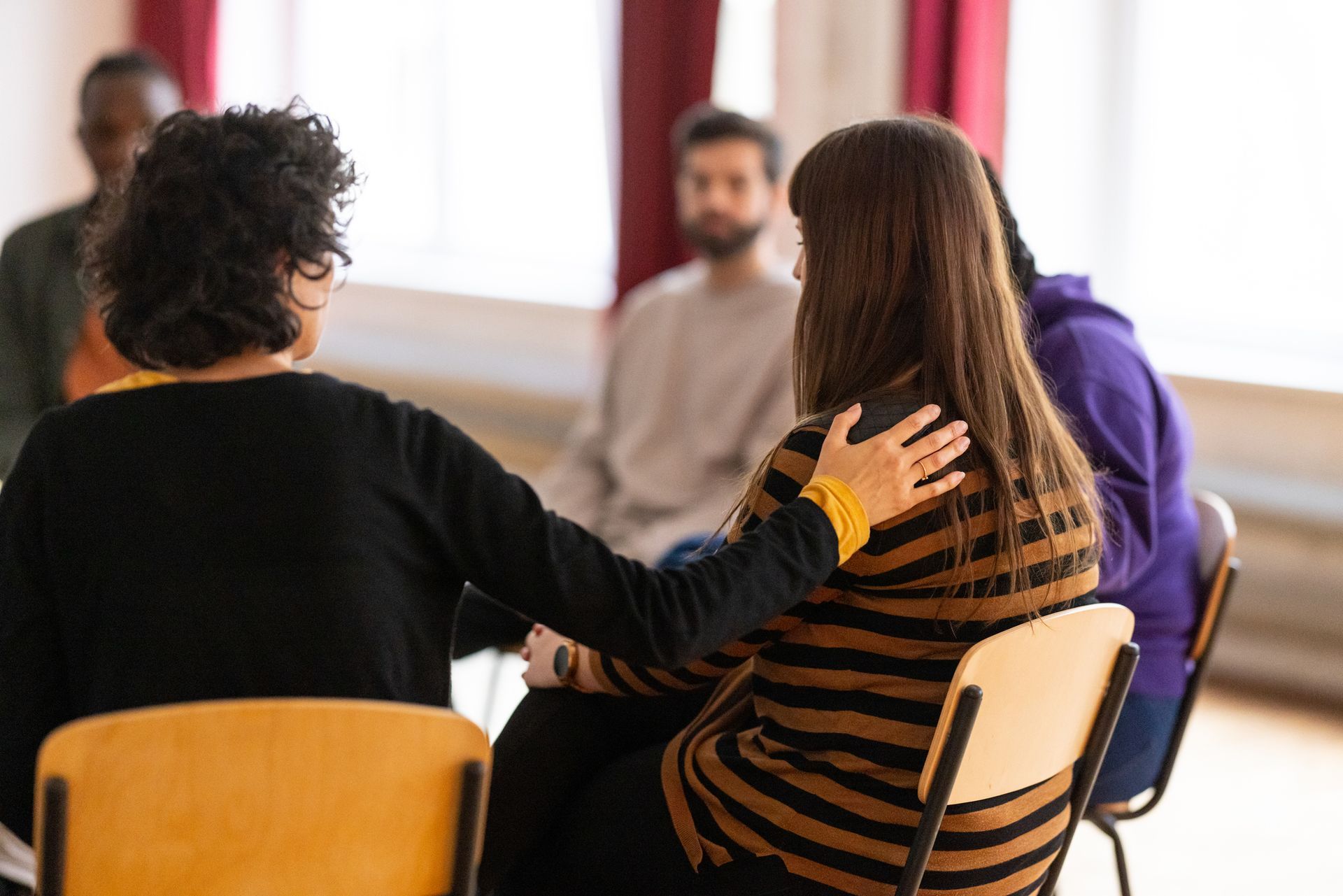 Woman comforts another in support group; others seated in a circle.
