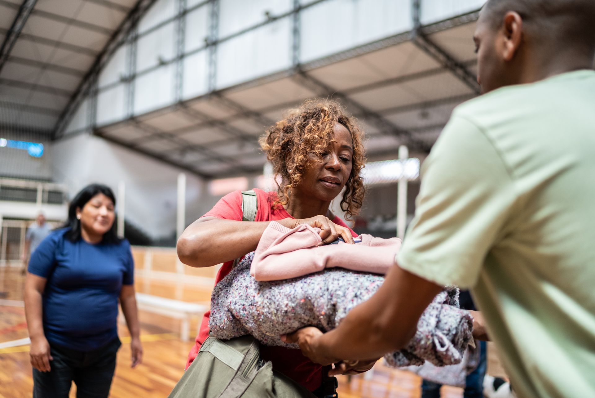 Woman receiving blankets from a man in a gymnasium; others stand by.
