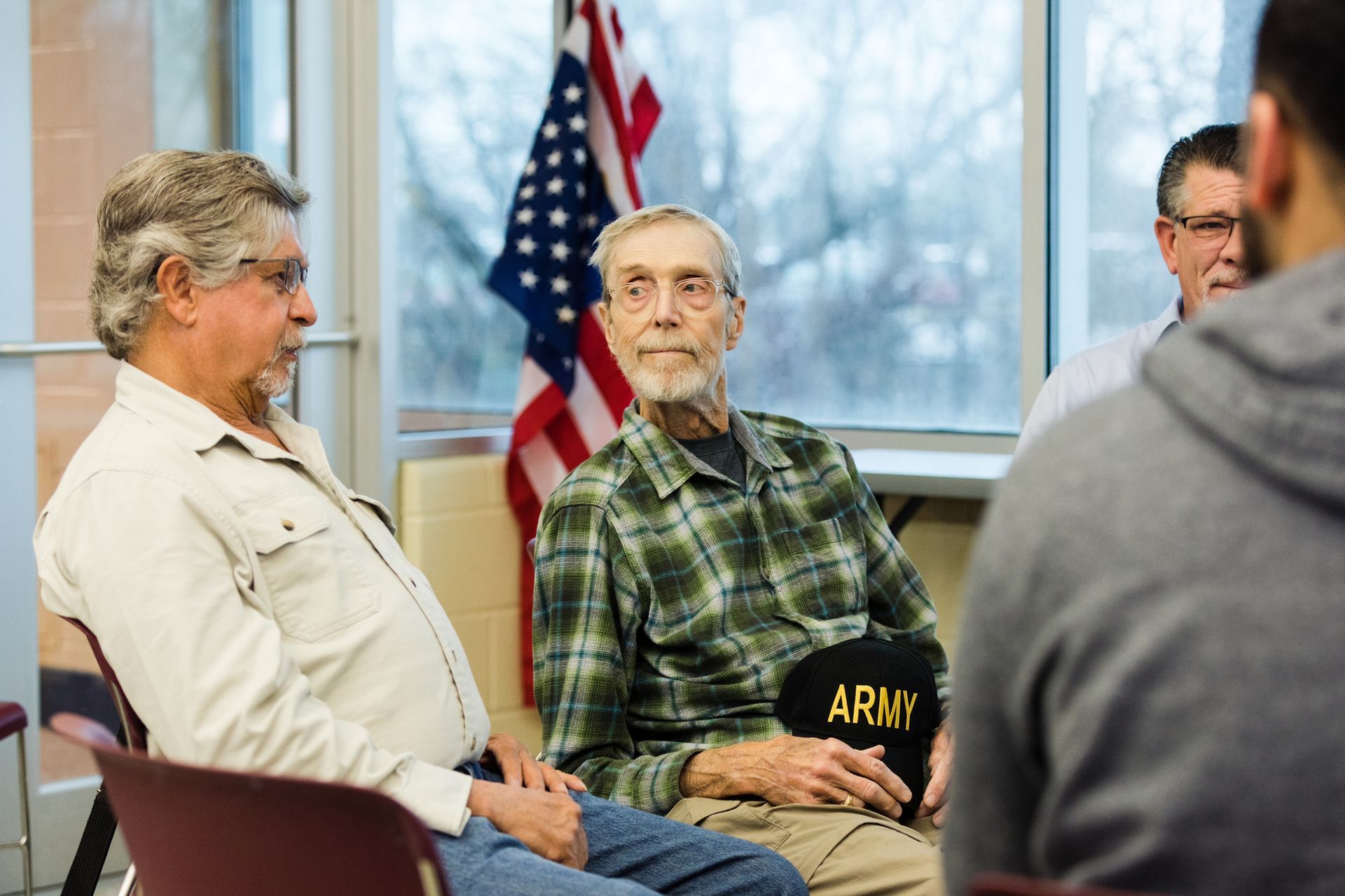 Veterans in a group meeting, seated in chairs, American flag in background.