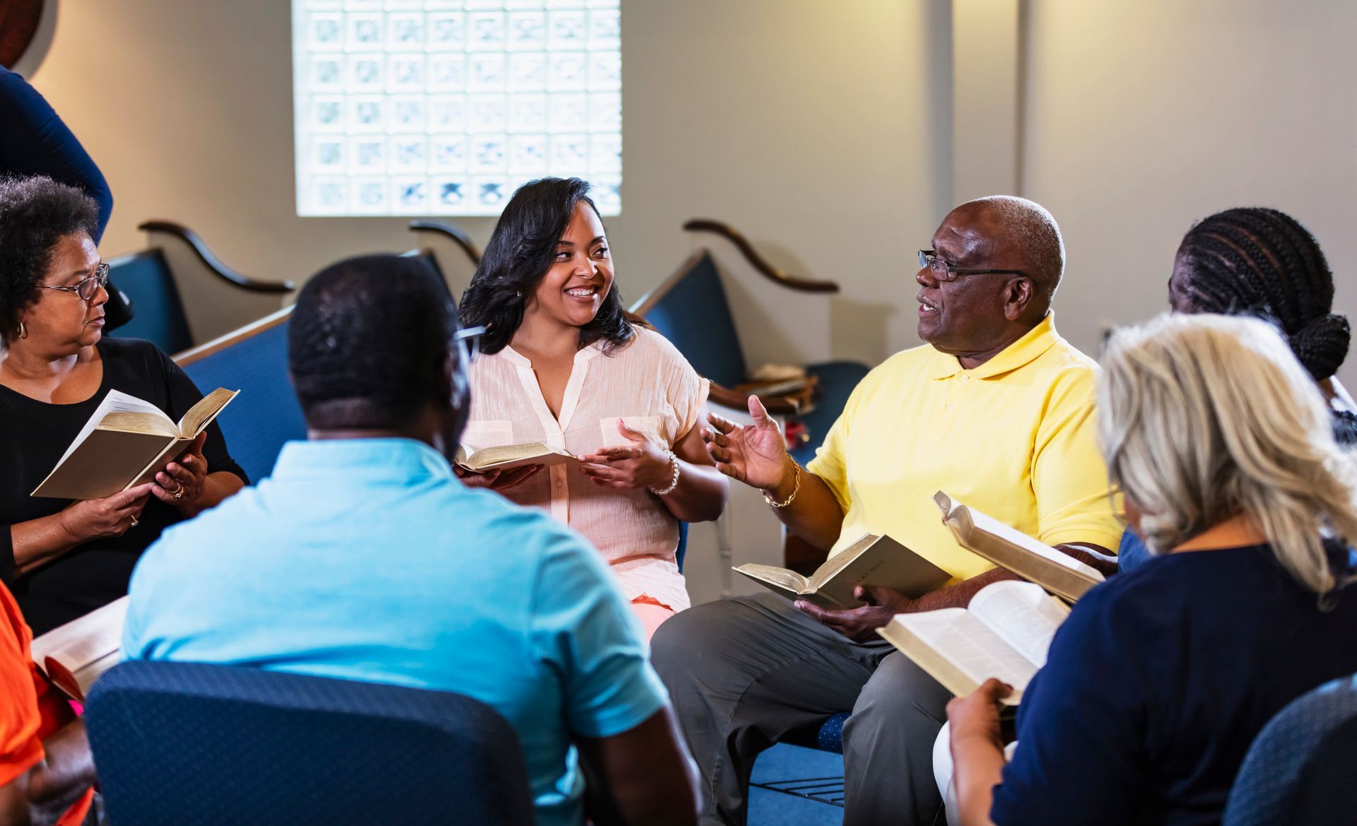 Group of diverse people in a circle, smiling, holding books, in a church-like setting.