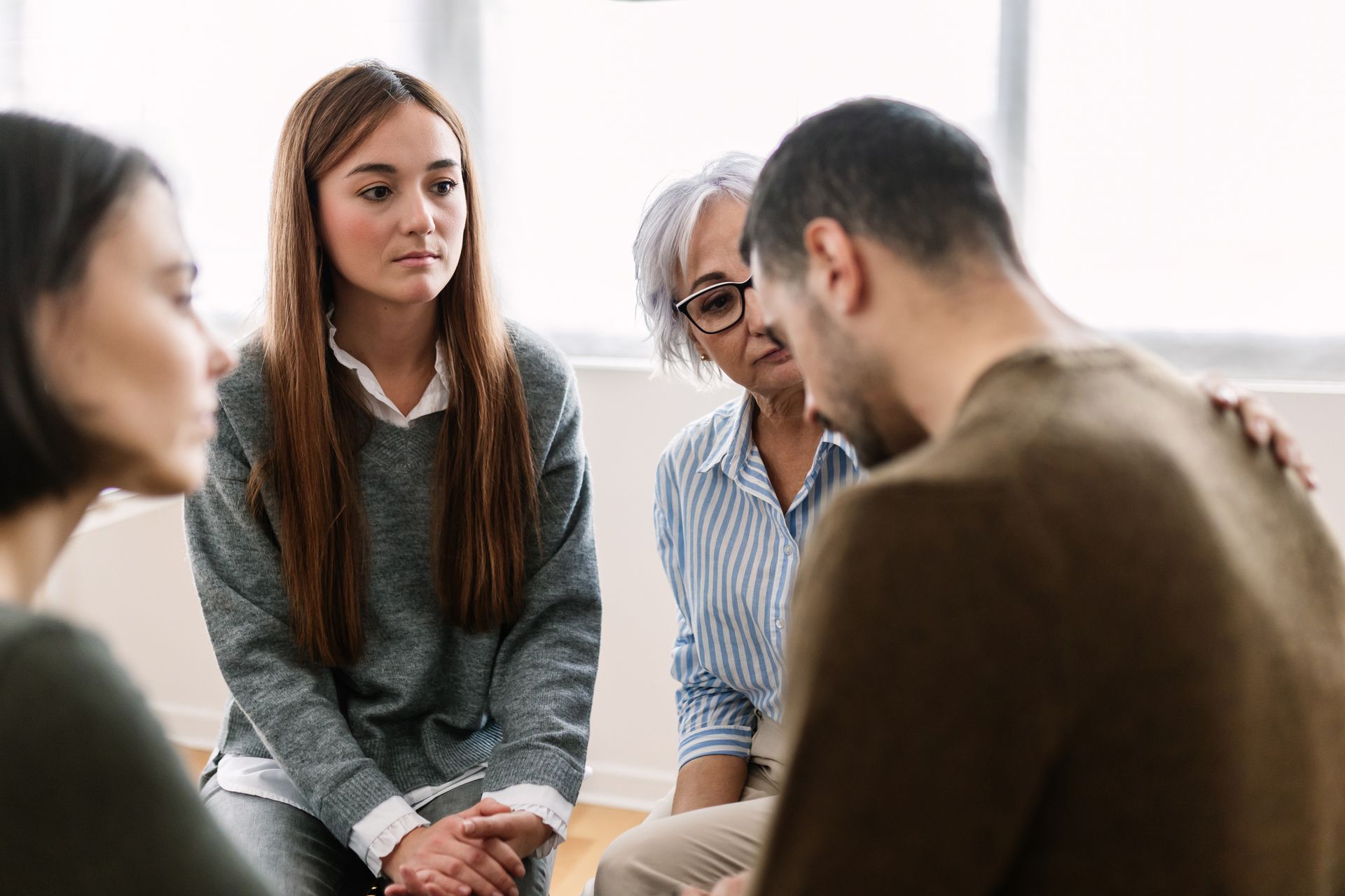 Group therapy session: People in a circle, one man comforted by others.