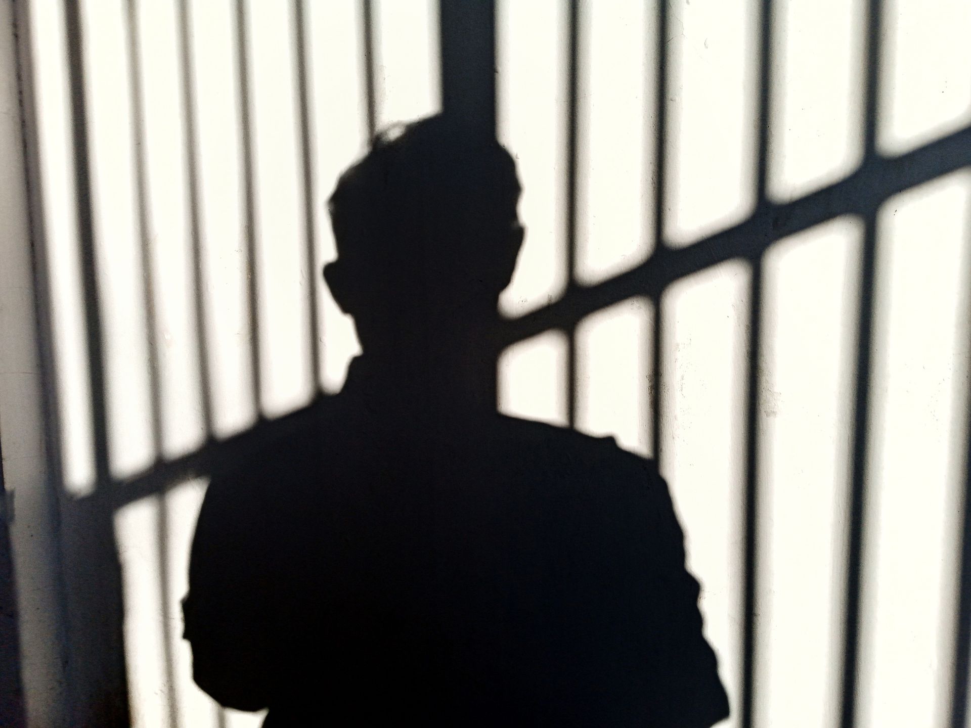 Silhouette of a person against a wall with shadows from barred windows.