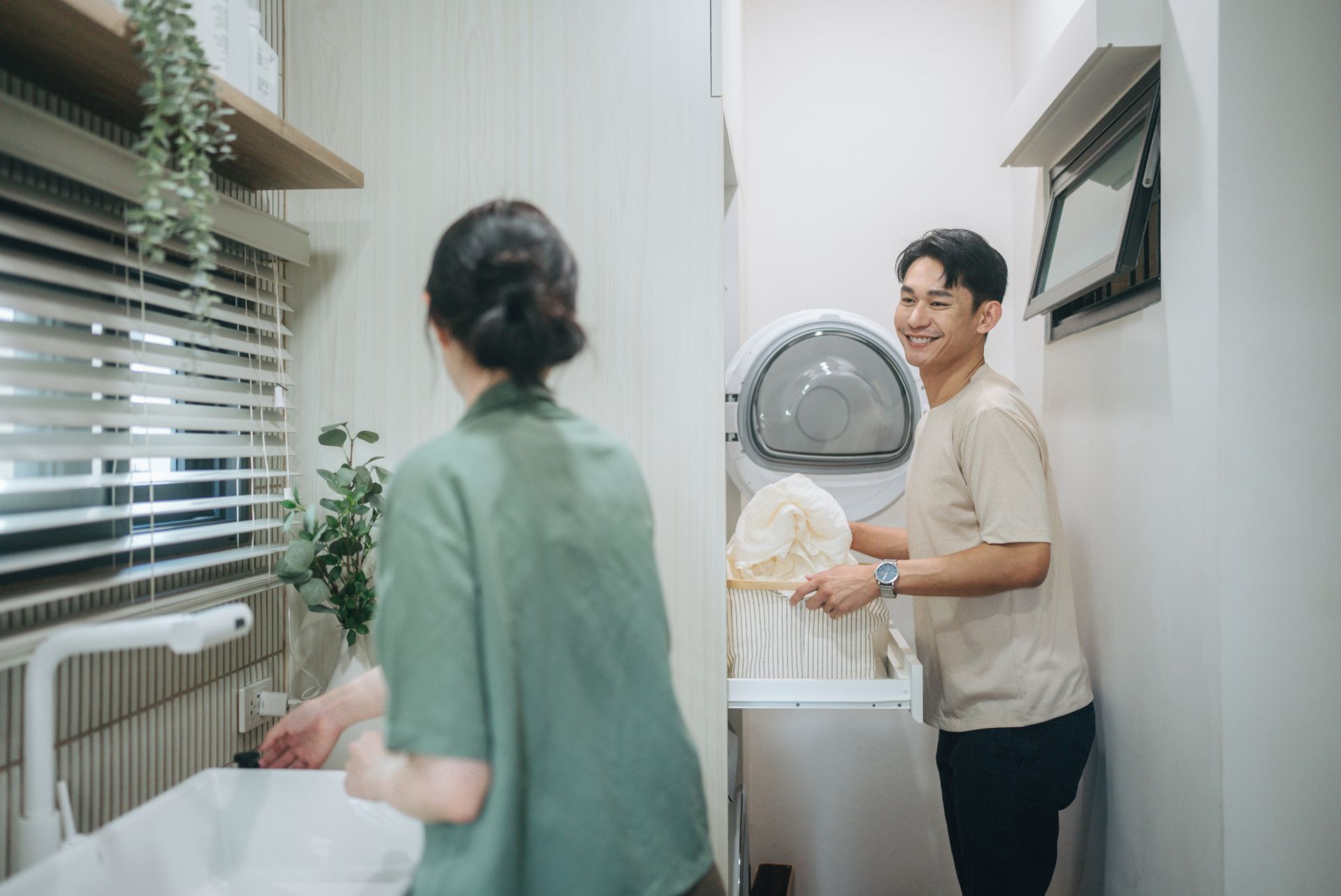 Woman in green shirt and man in tan shirt doing laundry in a well-lit laundry room.