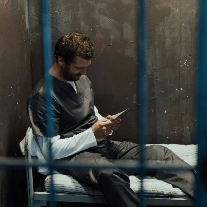 People greeting at a gated doorway. Smiling woman talks to a man; older couple waits inside.