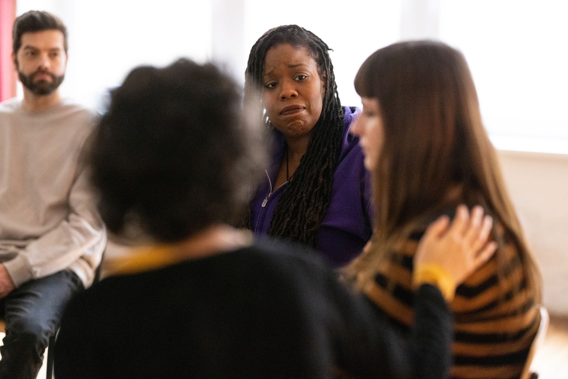 People in a circle, woman with braids appears distressed as another woman comforts her. Man and woman observe.
