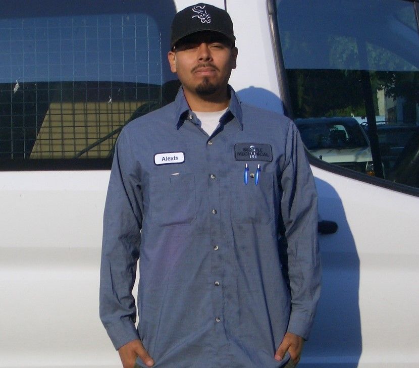 A man wearing a blue shirt and a black hat stands in front of a white van