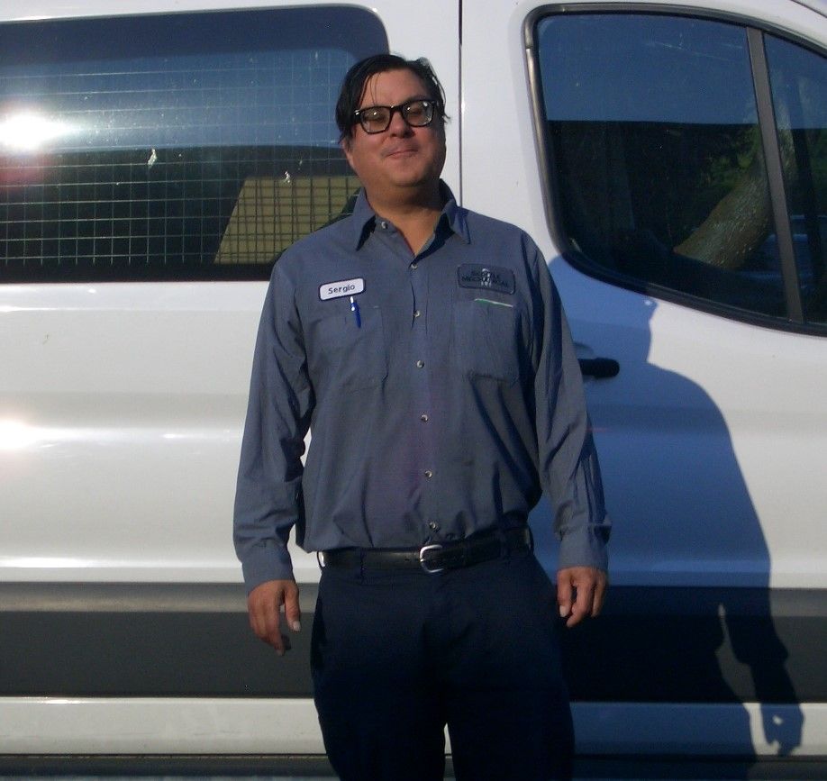 A man wearing glasses stands in front of a white van