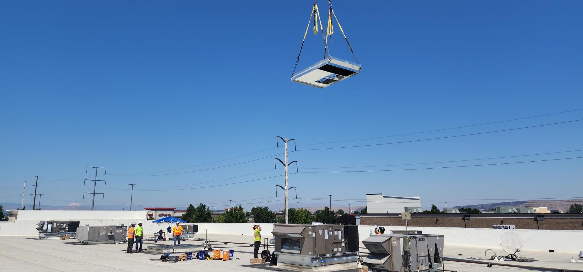 A crane is lifting a piece of equipment from the roof of a building.