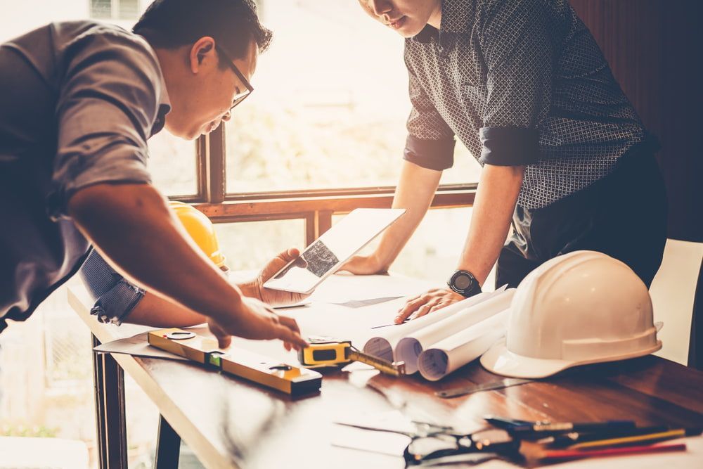 Two Men Are Looking At A Blueprint On A Table — Greg Pollard Building In Banora Point, NSW
