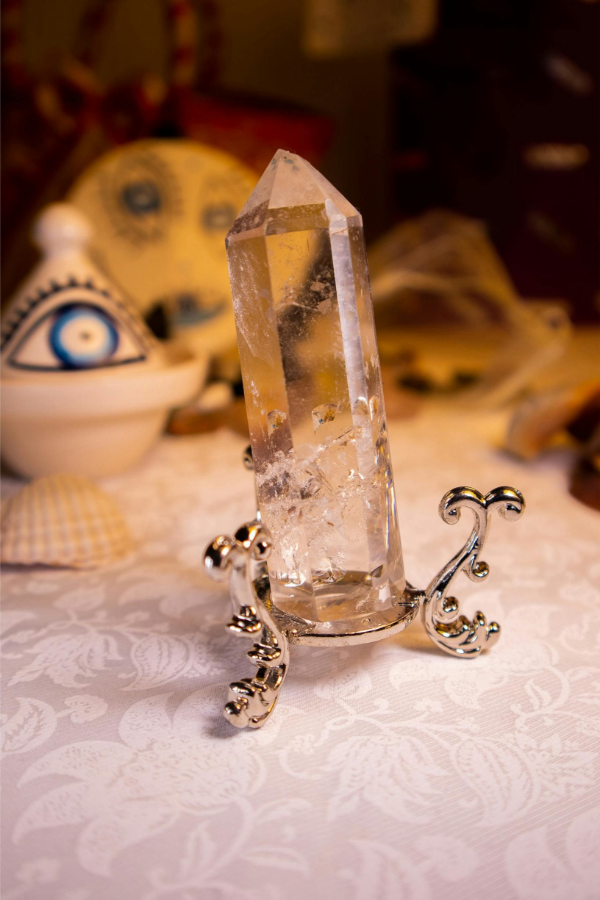 Clear crystal point in ornate silver holder on a patterned tablecloth, with a blurred decorative eye in the background