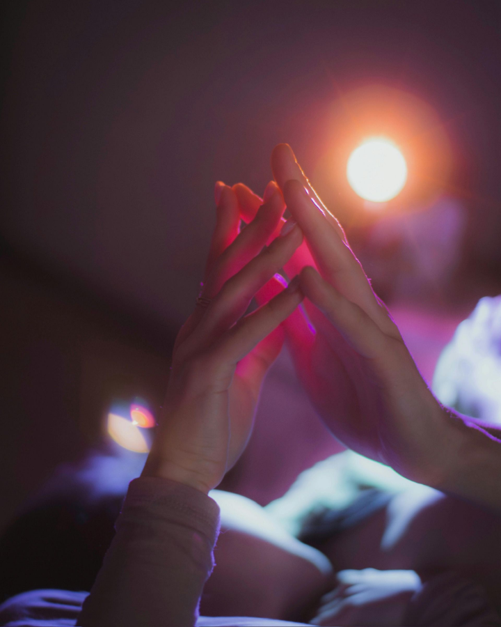 Two hands reaching toward each other under a glowing orange light in a dim room
