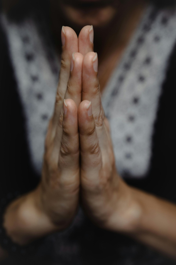 Hands pressed together in a prayer gesture against a blurred background