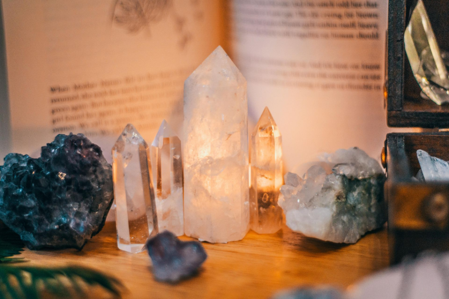 Assorted clear and dark crystals arranged on a wooden table, softly lit against an open book background