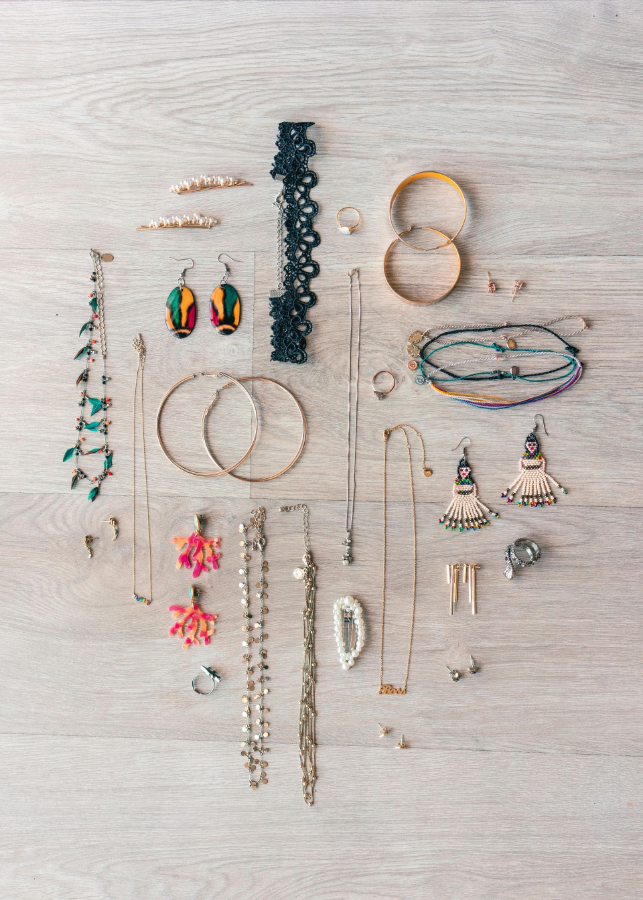 Assorted handmade earrings and jewelry laid out on a light wood surface.