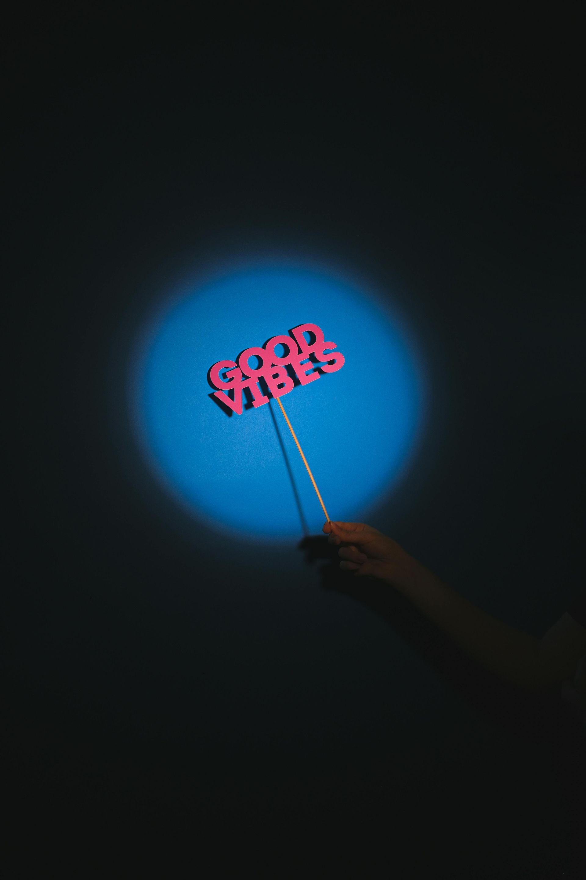 Hand holding a pink word sign glowing in a blue spotlight on a dark background