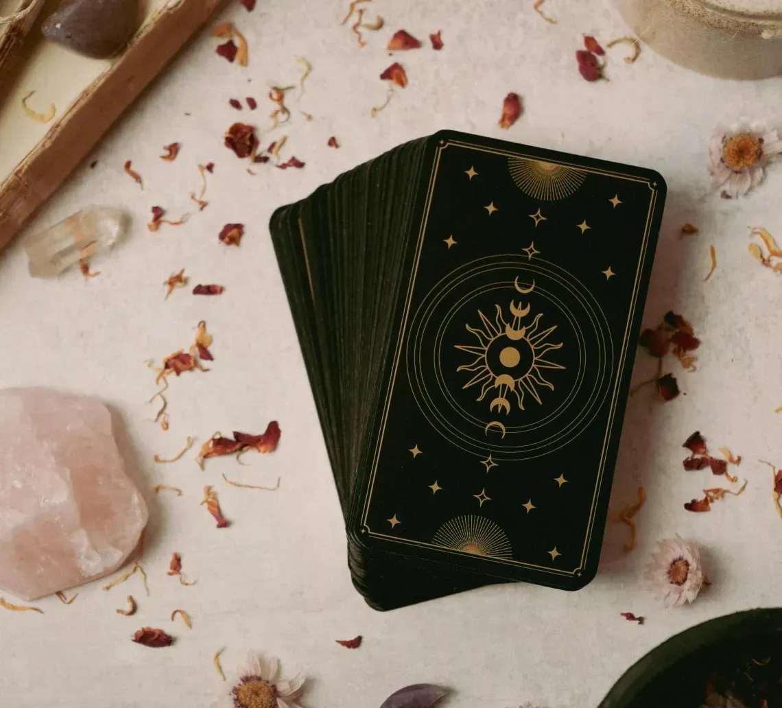 Dark green tarot cards on a tabletop with crystals, candles, and scattered dried petals