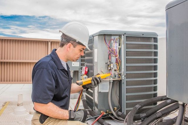 Technician inspecting rooftop HVAC unit with a multimeter and wires