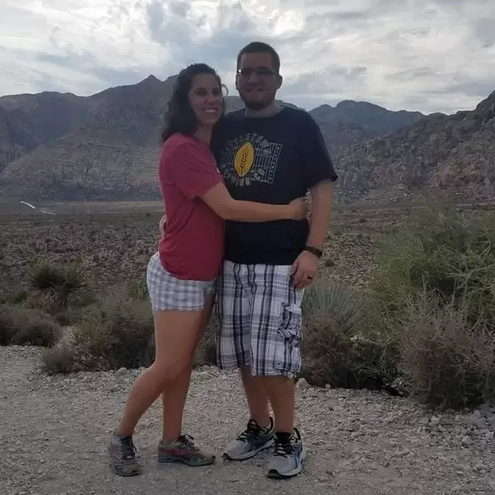 Couple hugging, posing for photo outdoors in front of mountains and desert landscape.
