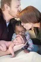 Family of four: parents kissing the heads of their daughters, one a baby, the other a toddler.