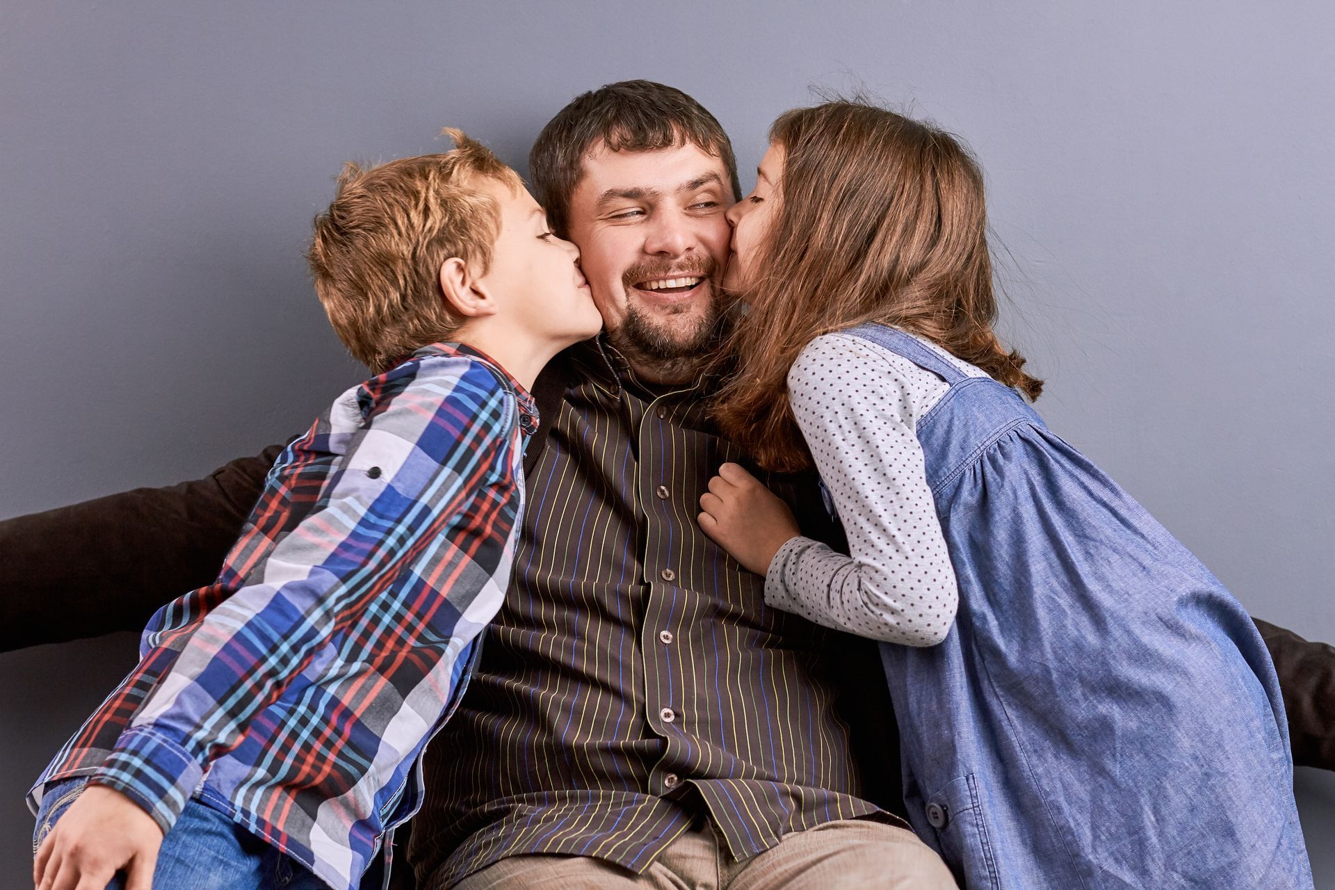 Man being kissed on both cheeks by two children, smiling against a gray backdrop.