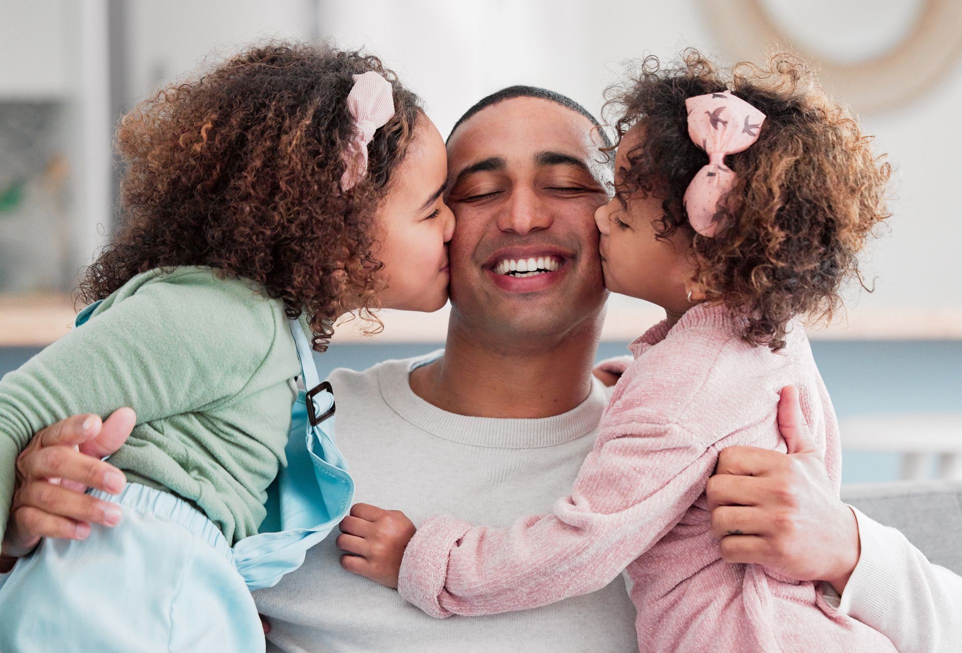 Father smiling as twin daughters kiss his cheeks.
