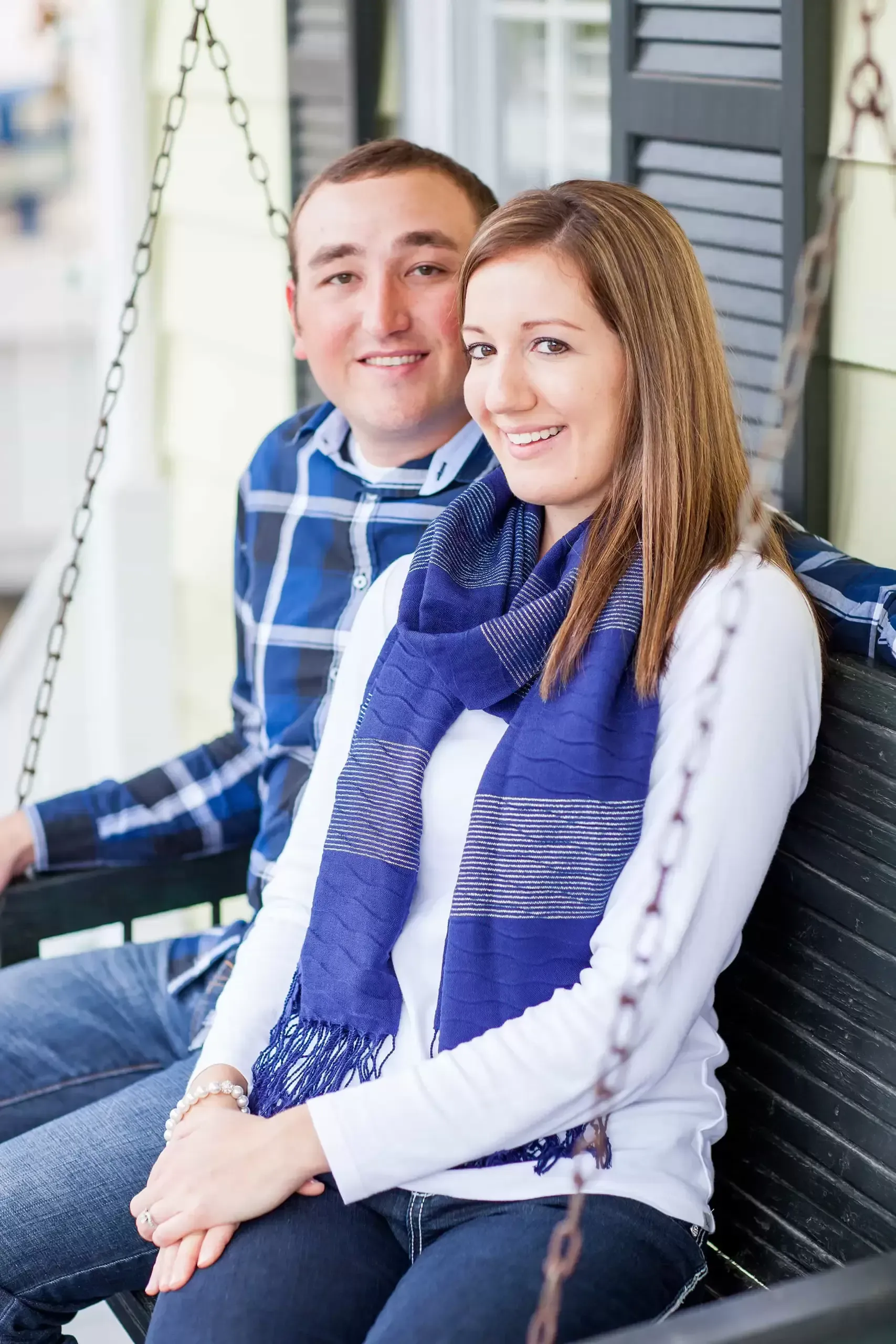 Couple on a porch swing, smiling. Woman in blue scarf, man in plaid shirt.