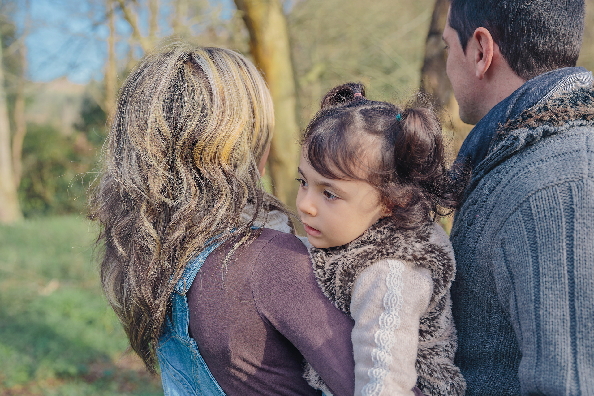 Father points upward, showing something to his child. They sit on a bench with teddy bears, red backdrop.