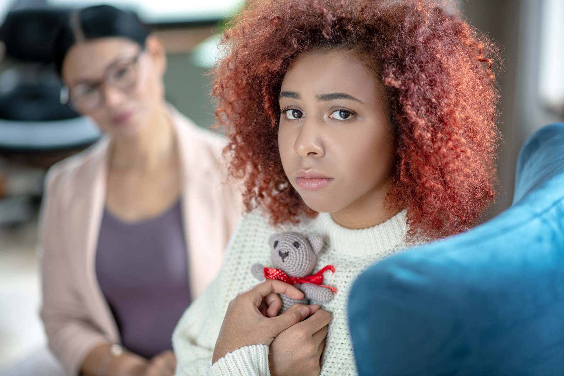 Father points upward, showing something to his child. They sit on a bench with teddy bears, red backdrop.