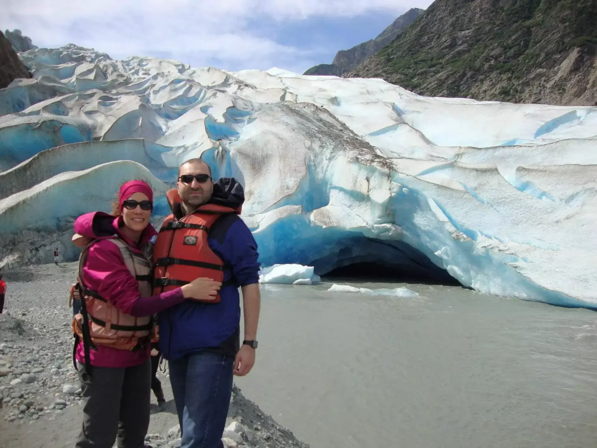 Couple in life vests poses in front of a blue glacier cave.